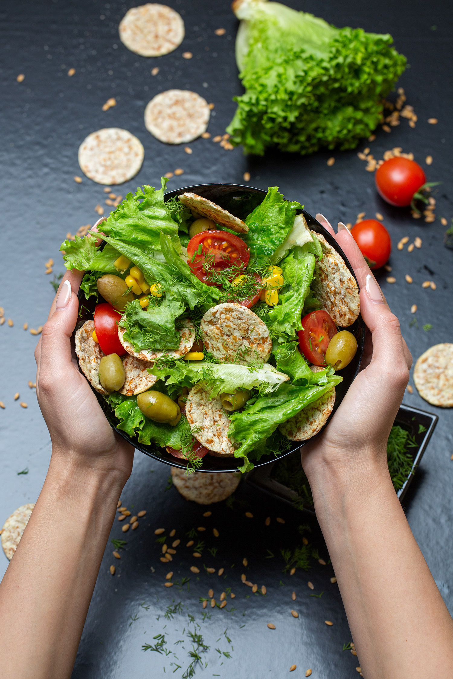 A vertical closeup of a person holding a bowl of salad with crackers and vegetables under the lights